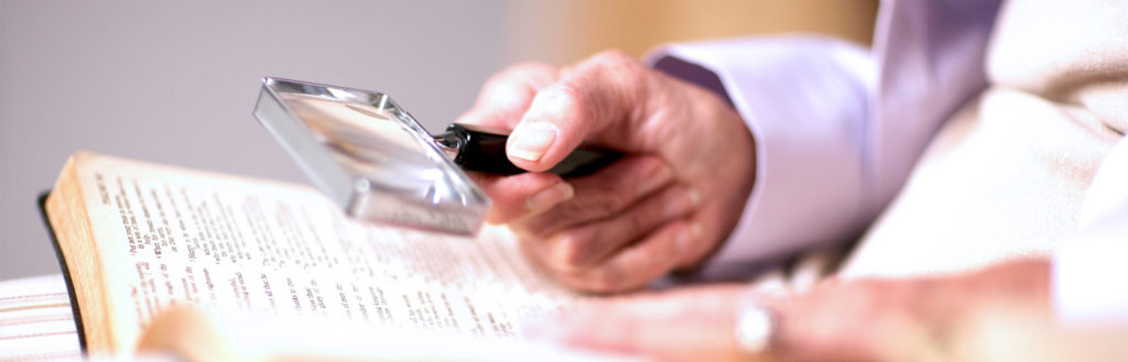 Man holding a handheld magnifier over a book using it to read. 